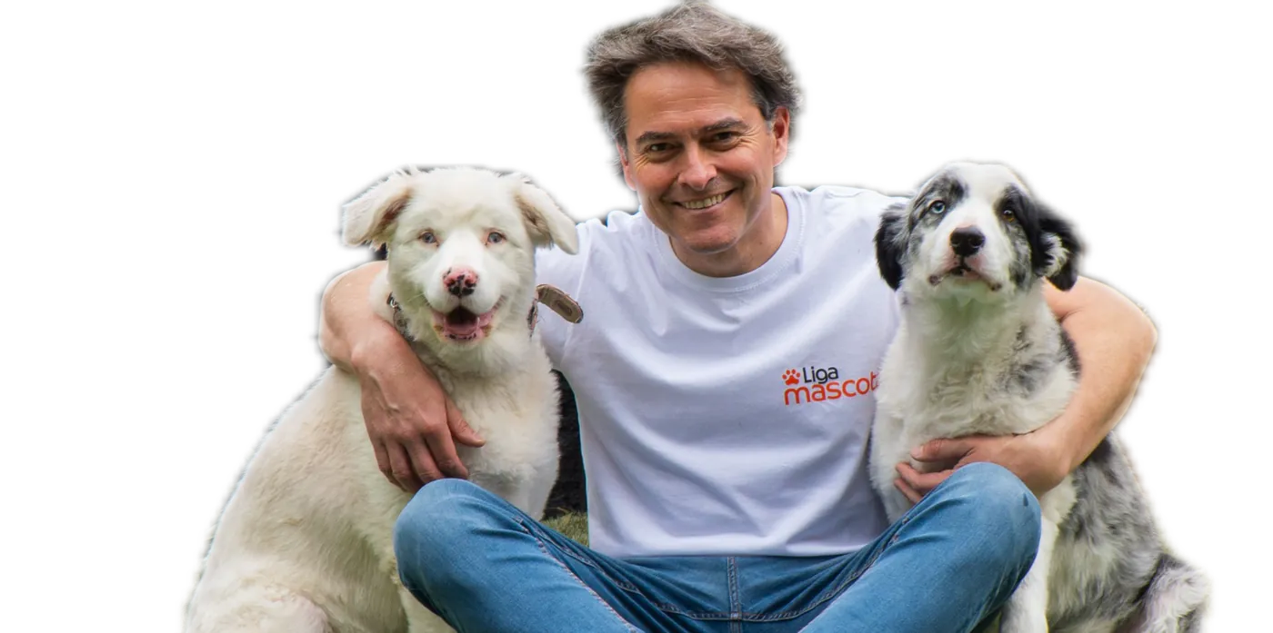 Sebastián Jiménez, director veterinario de Liga Mascotas, sentado en el pasto abrazando a un perro blanco y a un border collie
